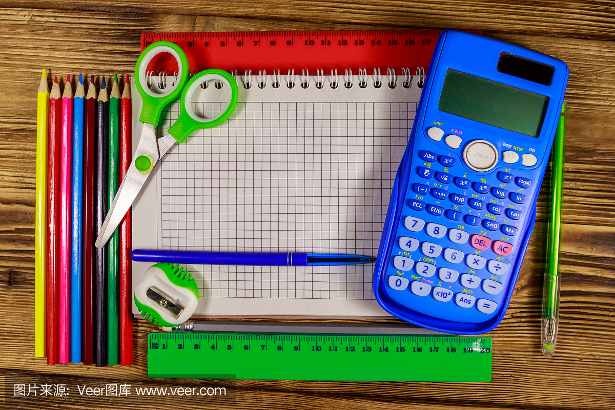 整套學(xué)校文具用品。空白記事本,計算器,尺子,鉛筆,鋼筆,剪刀和卷筆刀放在木桌上。俯視圖
